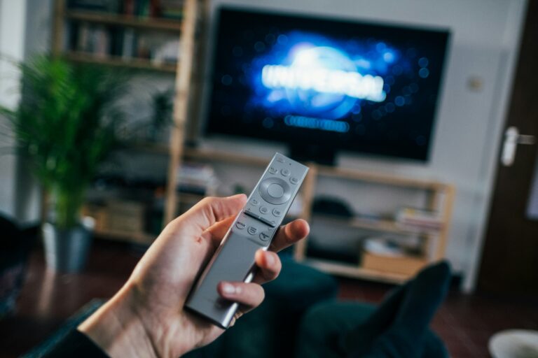 Person holding a remote control while watching a movie on a smart TV at home, illustrating IPTV Nordic streaming experience.